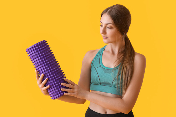 Young woman with purple foam roller on yellow background - Foto, immagini