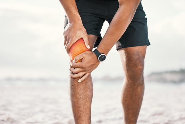 The time to get fit is running out. an unrecognizable male athlete holding his knee in pain while exercising on the beach - Foto, Imagen