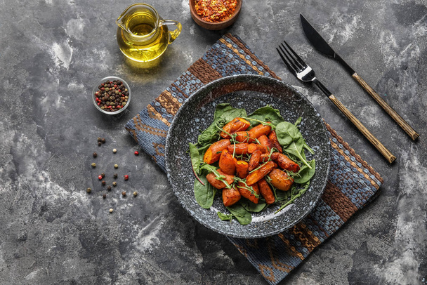 Composition with plate of tasty baked carrots and spices on grunge background - Photo, image