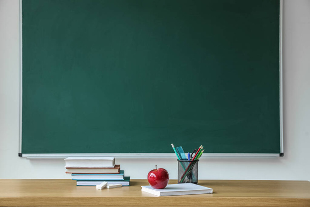 Apple with school books and pen cup on table near chalkboard - Фото, изображение