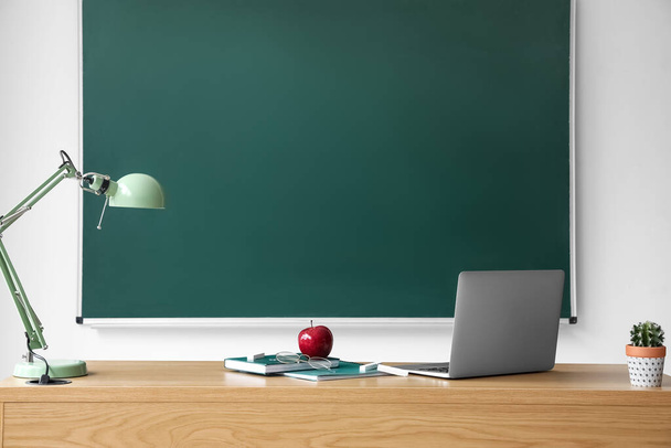 Apple with books, eyeglasses, laptop and lamp on table near chalkboard - Foto, Bild