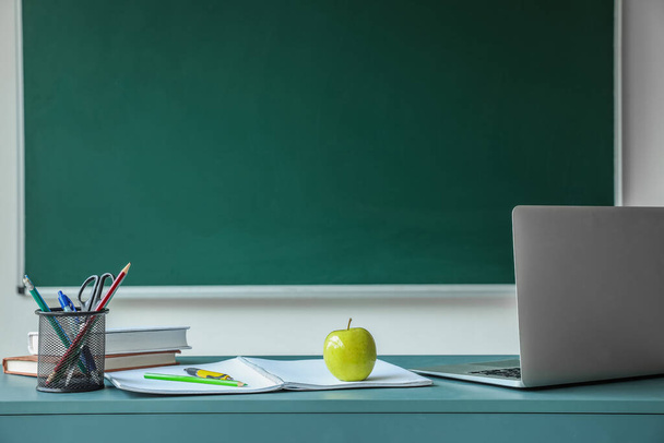 Apple with books, pen cup and laptop on table near school chalkboard - Zdjęcie, obraz
