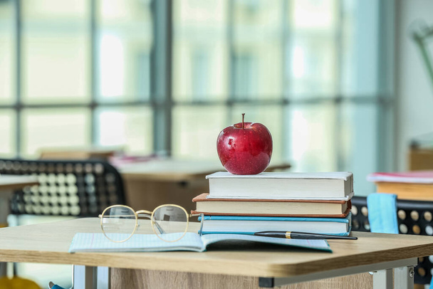 Apple mit Schulbüchern und Brillen auf dem Tisch im Klassenzimmer - Foto, Bild