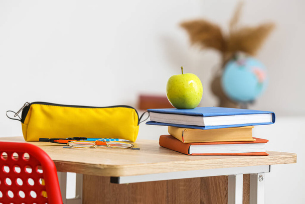Apple with school books and pencil case on table in classroom - Foto, afbeelding