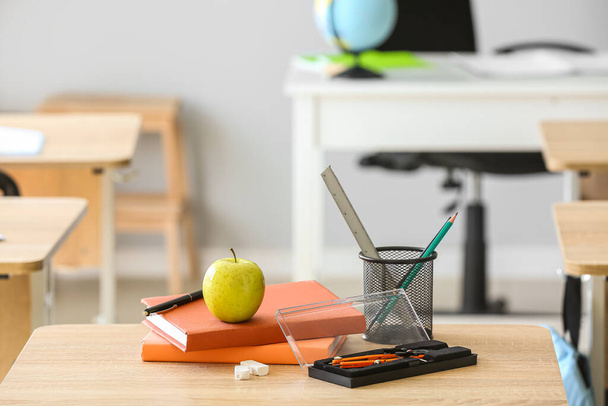 Jabłko z książkami, kubek na pióro i szkolna papeteria na stole w klasie - Zdjęcie, obraz