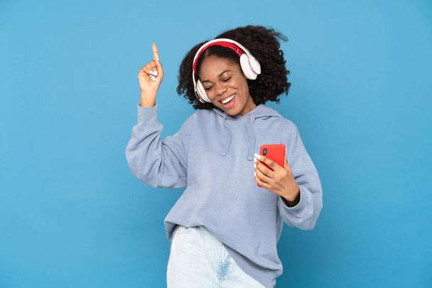 Young black woman using mobile phone while pointing finger upward isolated over white background - Fotó, kép