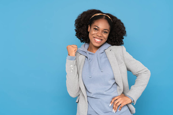 Young black woman wearing jacket smiling while making winner gesture isolated over blue background - Valokuva, kuva