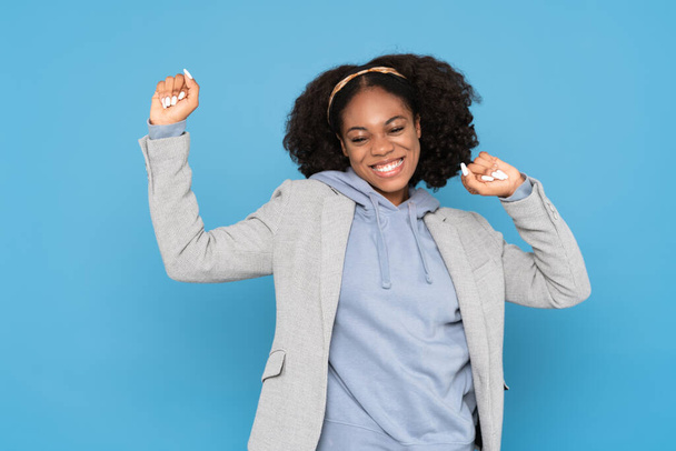 Young black woman wearing headband smiling while dancing isolated over blue background - Photo, image
