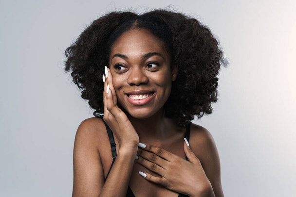 Young black woman in bra smiling and touching her cheek isolated over white background - Foto, Bild
