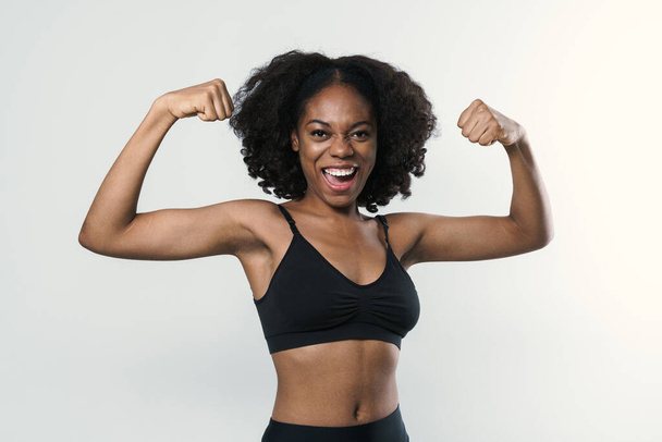 Young black woman in sportswear laughing and showing her biceps isolated over white background - Foto, imagen