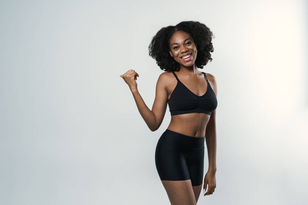 Young black woman in sportswear laughing while pointing finger aside isolated over white background - Foto, Imagem
