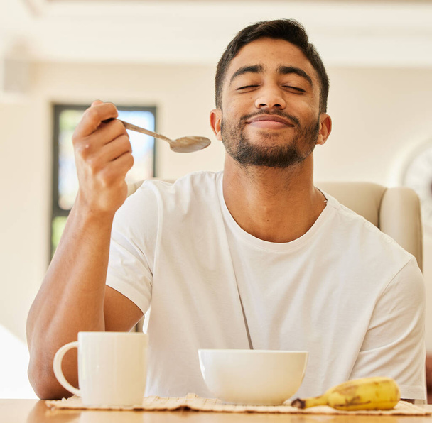 To jest przepyszne. przystojny młody mężczyzna siedzi sam i je śniadanie w domu - Zdjęcie, obraz