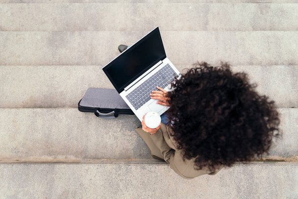 top view of an unrecognizable woman working with laptop computer sitting outdoors on a staircase, concept of business and urban lifestyle, copy space for text - Fotó, kép