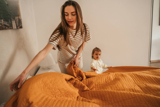 Young woman and a little girl standing in the bedroom and pulling the bedspread down - Foto, immagini