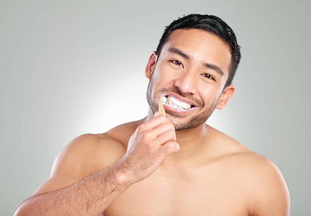 Stay clean, stay smiling. Studio shot of a handsome young man brushing his teeth against a grey background - 写真・画像