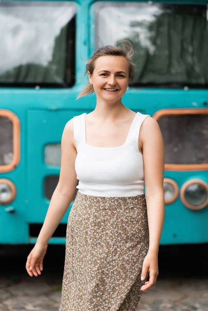 Улыбающаяся красивая блондинка стоит рядом со старым школьным автобусом и смотрит в камеру. Концепция образа жизни - Фото, изображение