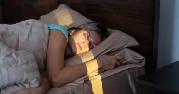Sunbeam shining on young sleeping woman in bedroom 4k movie. Morning awakening concept - Filmati, video