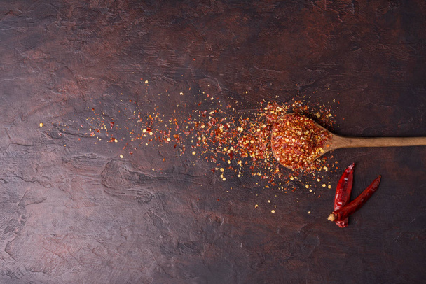 Chile seco o pimienta de cayena en una cuchara de madera colocada sobre un fondo oscuro con espacio para copiar, vista superior - Foto, imagen
