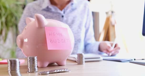 Pink sticker home budget hanging on piggy bank with coins closeup 4k movie. Family bookkeeping concept - Πλάνα, βίντεο