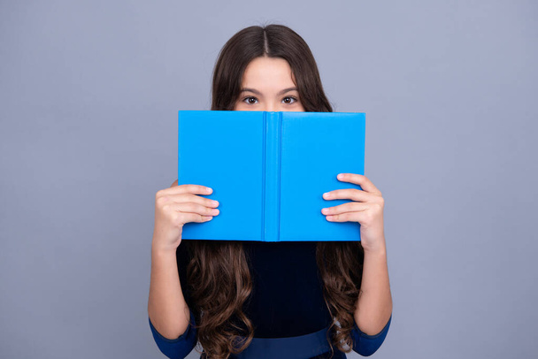 Schoolchild, teenage student girl hold book near eyes on gray isolated studio background. School and education concept. Back to school. Face hidden with book - Foto, Imagem
