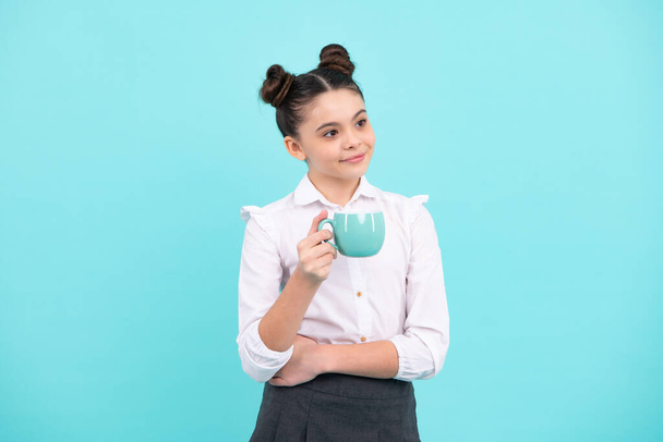 Genç kız elinde bir fincan sıcak kahve ya da çay tutuyor. Mavi arka planda fincanı olan çocuk, sabah enerji içeceği - Fotoğraf, Görsel