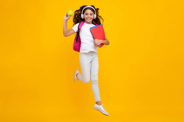 Schoolgirl, teenage student girl in headphones hold books on yellow isolated studio background. School and music education concept. Back to school - Foto, imagen