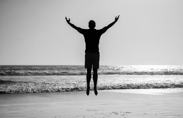 чувствовать свободу. молодой и свободный. спортсмен прыгает в океан. утренняя тренировка. здоровый мужчина силуэт поднял руки на пляже. энергичное лето. - Фото, изображение