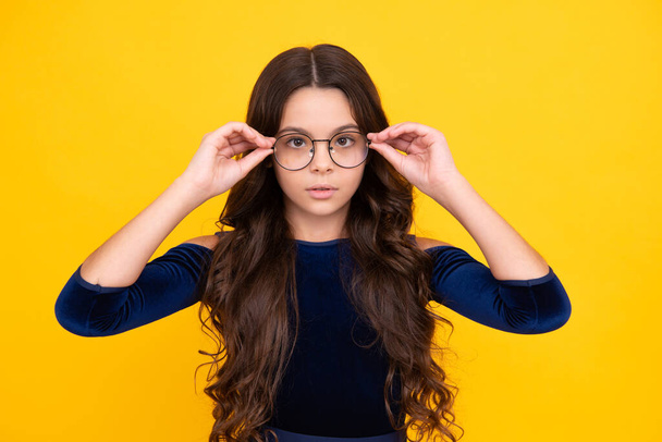 Tennager child girl wear eyeglasses looking at camera with confidence over yellow background, copy space. Kid get eyesight - Фото, изображение