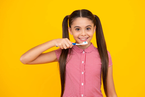 Teenager girl brushing her teeth over isolated yellow background. Daily hygiene teen child hold toothbrush, morning routine. Dental health oral care. Happy teenager, positive and smiling - Zdjęcie, obraz