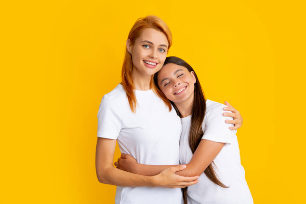 Mother and daughter teenager girl in t-shirt embrace cudding isolated on yellow color background studio. Mothers day love family - Foto, Imagen