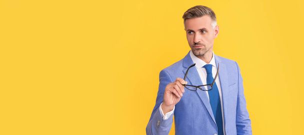 mature businessman in elegant jacket hold eyeglasses on yellow background, vision. Man face portrait, banner with copy space - 写真・画像