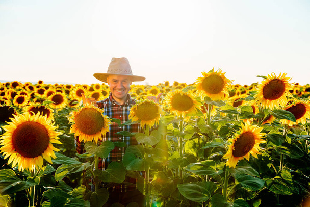 A smiling young farmer stands in a field and smiles happy looking at camera. The man is satisfied with his work. A happy joyful on his face. The working day, the bright sun is shining. copy space - Foto, Imagem