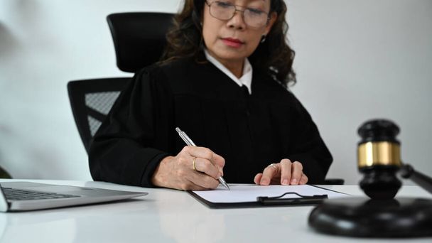 Profesjonalna prawniczka podpisująca papiery młotkiem na białym stole. Prawnik, wymiar sprawiedliwości i prawo, koncepcja adwokata. - Zdjęcie, obraz