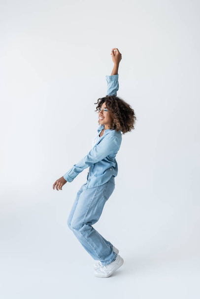 side view of joyful african american woman posing in denim clothes with arm up on grey background - Fotografie, Obrázek
