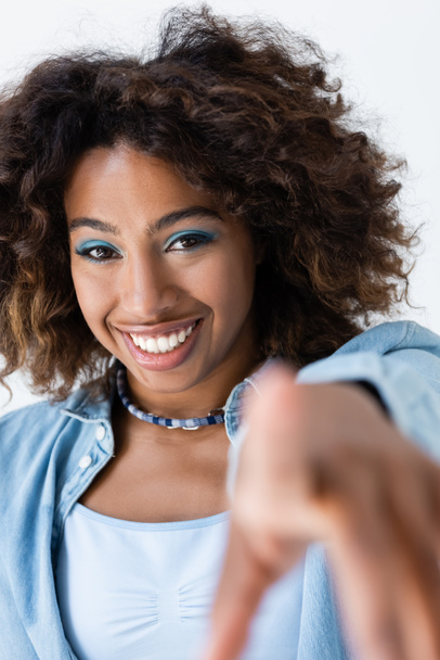 happy african american woman with wavy hair looking at camera and pointing with finger isolated on grey - Photo, image