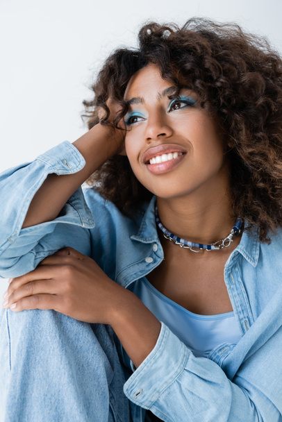 joyful african american woman in beads and blue denim shirt looking away isolated on grey - Foto, immagini