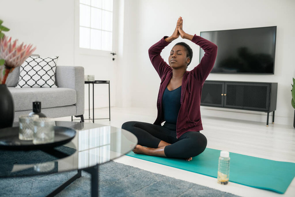 Fekete afrikai nő ül jóga póz szőnyegen a nappaliban, nyújtás és meditáció otthon edzés - Fotó, kép