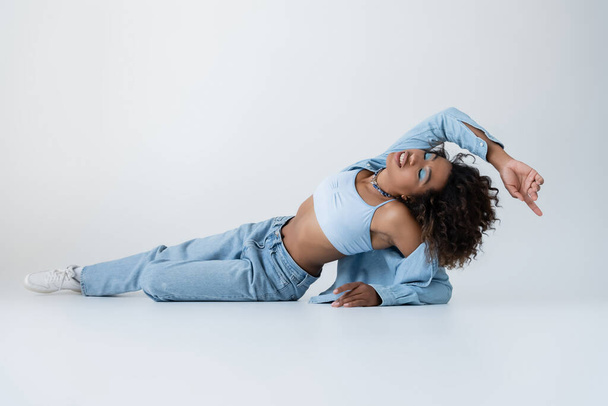 full length of sensual african american woman in white crop top and jeans lying with closed eyes on grey background - Φωτογραφία, εικόνα