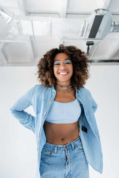 happy african american woman in blue denim shirt and white crop top on white background - Photo, image