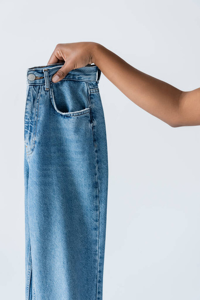 partial view of african american woman showing blue cotton jeans isolated on grey - Foto, imagen