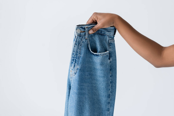 partial view of african american woman holding blue cotton jeans isolated on grey - Foto, Imagem