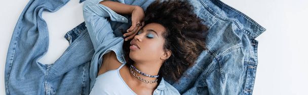 top view of african american woman with closed eyes lying near denim clothing on grey background, banner - Fotografie, Obrázek