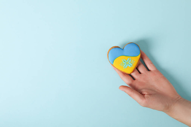 Female hand holds cookie with Ukraine flag colors on blue background - Foto, imagen