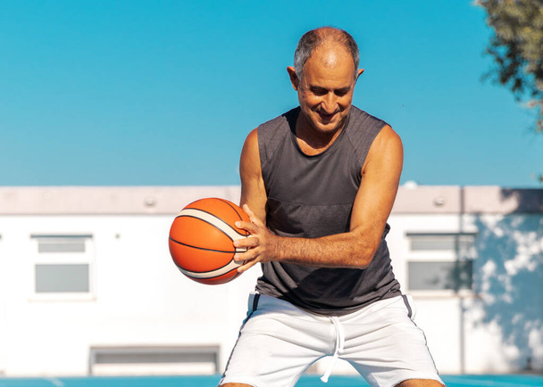 Close-up portret van Turks-Cypriotische senior volwassen atleet spelen basketbal buiten in de zomer zonnige dag. - Foto, afbeelding