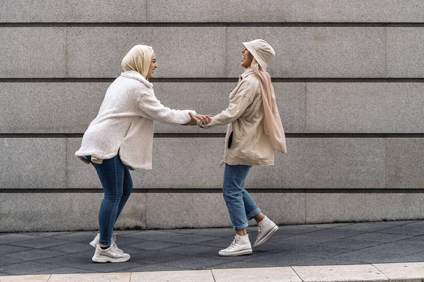 Affective young women wearing hijab laughing and walking in the street. - Foto, imagen