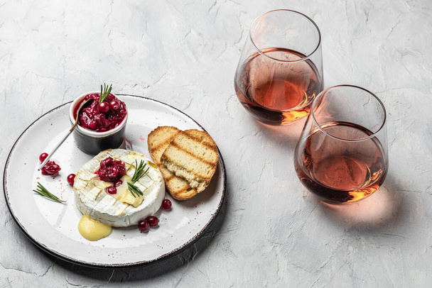 Γαλλική κουζίνα. Ψημένο τυρί καμαμπέρ με cranberries και φύλλα βασιλικού, κρασί σε ελαφρύ φόντο, banner, μενού, μέρος συνταγής για κείμενο. - Φωτογραφία, εικόνα