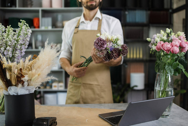 Small flower business. Cropped view of man working in flower shop. Hand of young man holding flowers are working with them in floral shop. - 写真・画像