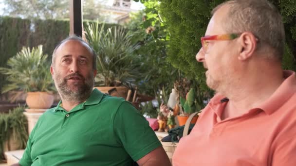 Positive middle aged men in casual clothes looking at each other while having conversation on backyard on summer day - Filmagem, Vídeo
