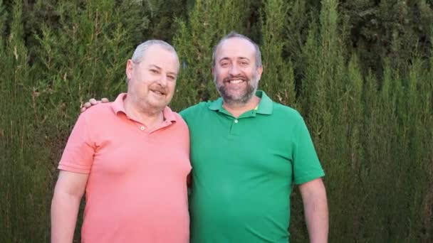 Happy middle-aged male couple smiling at camera while standing together outdoors. Slow motion video. LGBT, love and relationship concept. - Metraje, vídeo