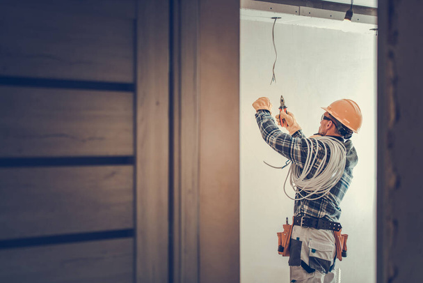 Fully Equipped Professional Electrician Working on Illumination Installation Cutting Cables Using His Wire Cutter. Residential House Renovation Work Theme. - 写真・画像